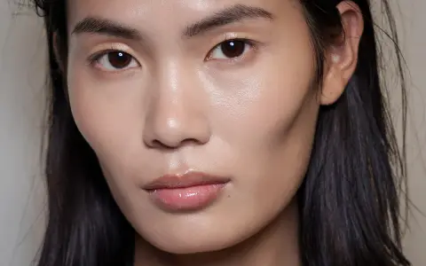 Ein Gesicht mit makellosem Teint und glänzenden Lippen. Das Make-up ist dezent, aber wirkungsvoll.