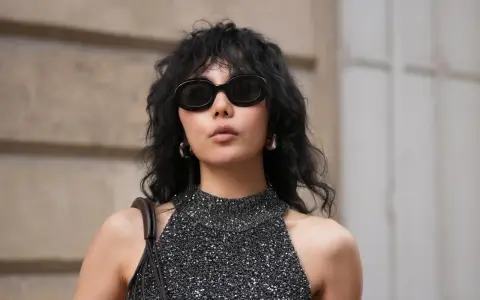 Frau mit schulterlangem Wolf Cut, Sonnenbrille und glitzerndem Top.