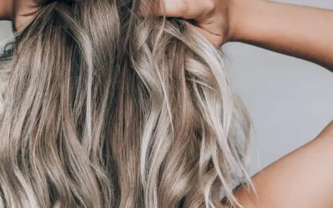 Hände im blonden, drahtigen Haar, das in Wellen fällt.