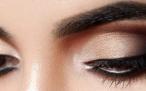 Nahaufnahme eines geschminkten Auges. Ein schimmernder Lidschatten wurde aufgetragen, mit einem dramatischen dunklen Smokey-Eye-Effekt.