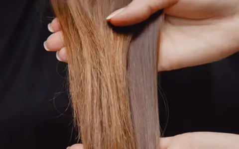 Hände halten zwei Strähnen Haar. Eine ist hellbraun und wirkt etwas struppig, die andere ist dunkler und glänzt. So bekomme ich glanz in meine haare.