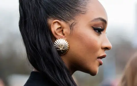 Ein scharfer Cat-Eye-Liner betont die Augen, perfekt aufgetragen mit Kajal. Goldene Muschel-Ohrringe und ein hoher Pferdeschwanz runden den Look ab.