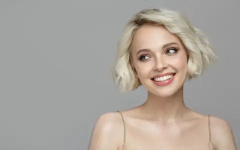 Lächelnde Frau mit sehr feinem Haar, das zu einem kurzen Bob gestylt ist. Ihre blauen Augen blicken nach links.