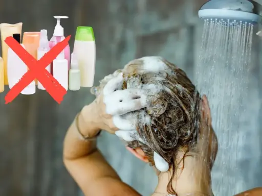 Frau wäscht sich die Haare unter der Dusche, Schaum im Haar. Eine rote durchgestrichene Gruppe von Shampoo-Flaschen deutet auf haare waschen ohne shampoo hin.