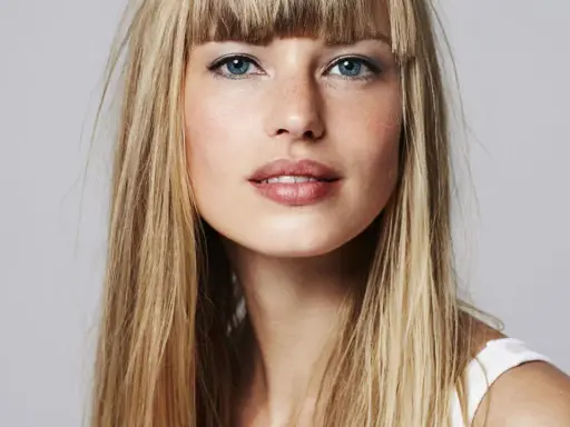 Blonde Frau mit auffälligem Buzz Cut und blauen Augen, die direkt in die Kamera blickt.