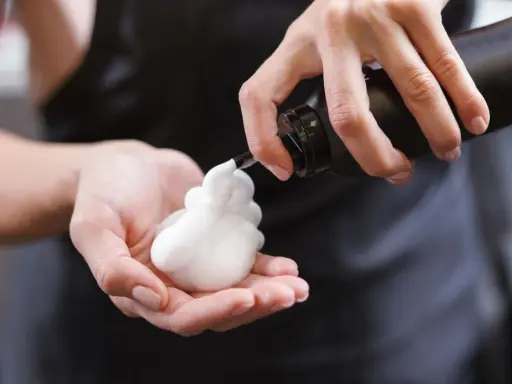 Schaumfestiger Anwendung: Eine Hand hält eine Flasche, aus der weißer Schaum in die andere Hand fließt.