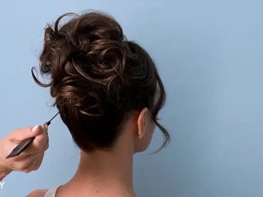 Eine Hand formt mit einem Kamm einen voluminösen, messy bun.
