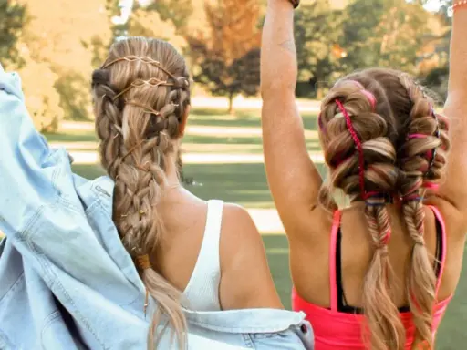 Zwei Freundinnen mit aufwendigen Festival Frisuren, Zöpfen mit Lederbändern und bunten Fäden, genießen die Sonne.