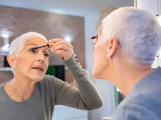 Frau über 60 schminkt sich die Wimpern, um Schlupflider zu kaschieren. Ein Tipp für ein strahlendes Augen-Make-up.