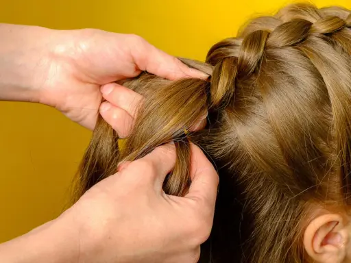 Hände flechten einen Bauernzopf. Die Haare werden sorgfältig zu einem kunstvollen Zopf geflochten, der an traditionelle Frisuren erinnert.