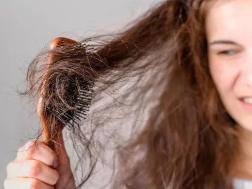 Verzweifelt versucht eine junge Frau, ihre strohigen Haare nach einer Keratinbehandlung zu kämmen. Die Bürste verheddert sich in den widerspenstigen Strähnen.