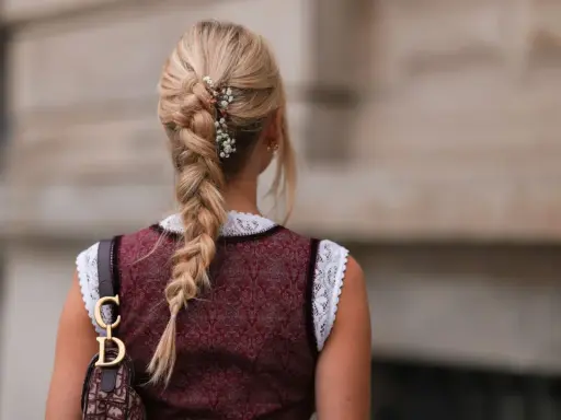 Blonde Zopf-Frisur mit Blumen-Akzenten, perfekt für Oktoberfest-Frisuren. Ein Dirndl und eine Dior-Tasche runden den Look ab.