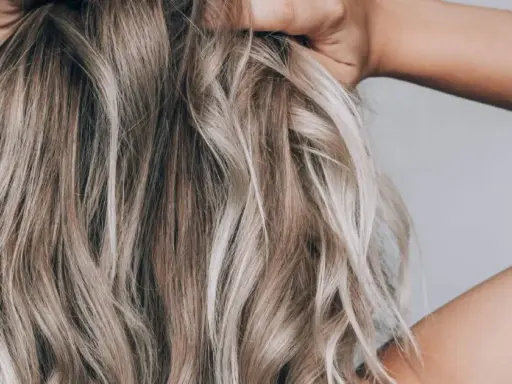 Hände im blonden, drahtigen Haar, das in Wellen fällt.