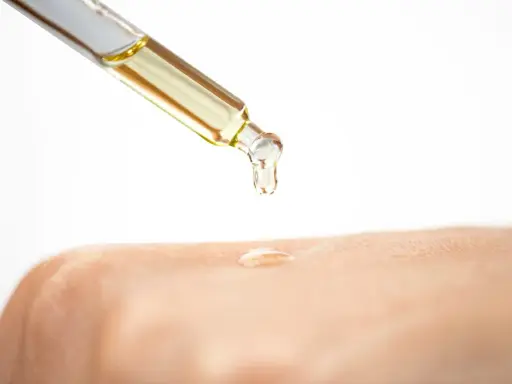 Ein Tropfen Öl fällt aus einer Pipette auf die Haut. Die Glycerin Wirkung auf die Haut wird hier gezeigt: Feuchtigkeit und Geschmeidigkeit.