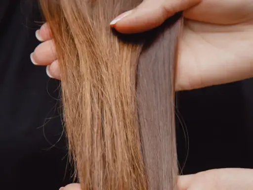 Hände halten zwei Strähnen Haar. Eine ist hellbraun und wirkt etwas struppig, die andere ist dunkler und glänzt. So bekomme ich glanz in meine haare.