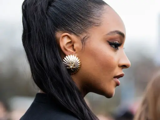 Ein scharfer Cat-Eye-Liner betont die Augen, perfekt aufgetragen mit Kajal. Goldene Muschel-Ohrringe und ein hoher Pferdeschwanz runden den Look ab.