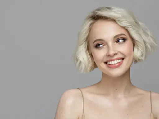 Lächelnde Frau mit sehr feinem Haar, das zu einem kurzen Bob gestylt ist. Ihre blauen Augen blicken nach links.