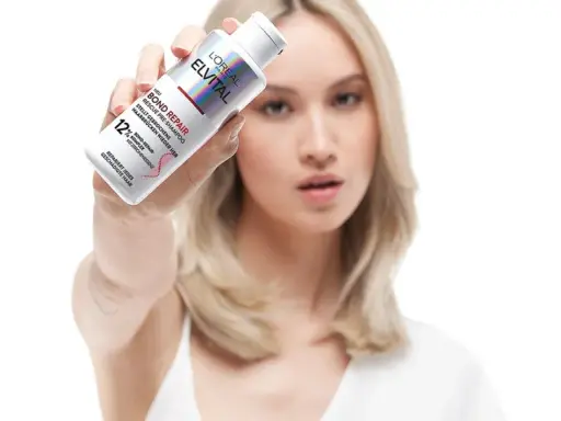 Frau hält L'Oréal Elvital Bond Repair Pre-Shampoo. Ideal für die Haarpflege bei trockenem Haar, repariert es geschädigte Haarbrücken.