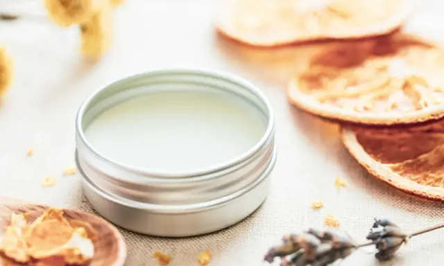 Ein Döschen mit selbstgemachtem Lippenbalsam, umgeben von getrockneten Orangen, Lavendel und Kräutern.