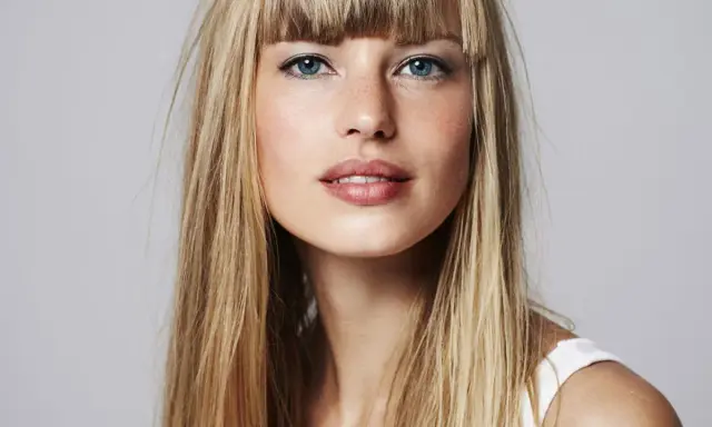 Blonde Frau mit auffälligem Buzz Cut und blauen Augen, die direkt in die Kamera blickt.