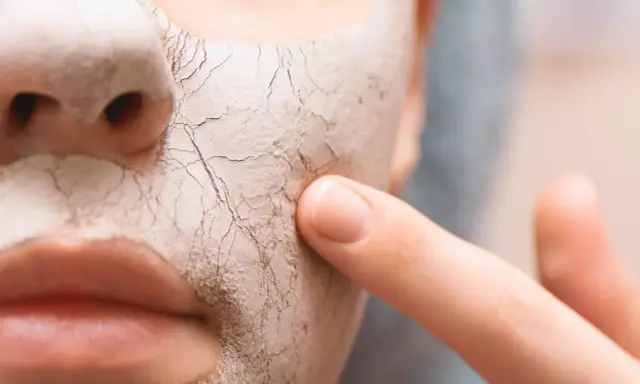 Nahaufnahme eines Gesichts mit einer trockenen, rissigen Maske. Ein Finger berührt sanft die Haut, um zu zeigen, wie man trockene Haut von innen behandeln kann.
