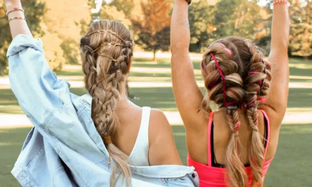 Zwei Freundinnen mit aufwendigen Festival Frisuren, Zöpfen mit Lederbändern und bunten Fäden, genießen die Sonne.