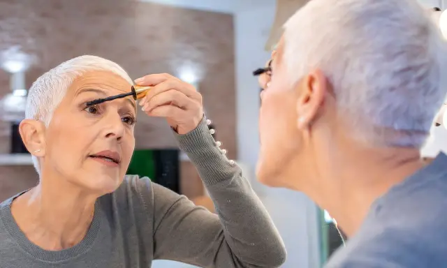 Frau über 60 schminkt sich die Wimpern, um Schlupflider zu kaschieren. Ein Tipp für ein strahlendes Augen-Make-up.