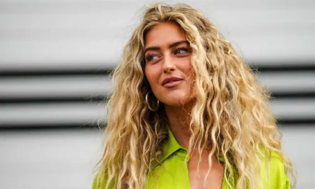Frauen mit voluminösen, welligen Haaren, die durch locken ohne hitze erzielt wurden. Sie trägt ein leuchtend grünes Hemd.