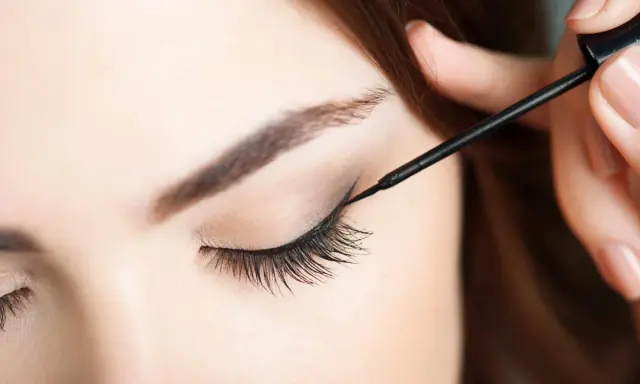 Eine Hand zieht mit schwarzem Eyeliner einen Wing für verführerische Cat Eyes.