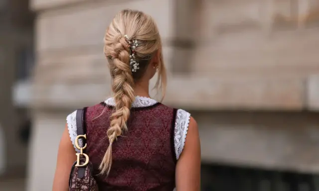 Blonde Zopf-Frisur mit Blumen-Akzenten, perfekt für Oktoberfest-Frisuren. Ein Dirndl und eine Dior-Tasche runden den Look ab.