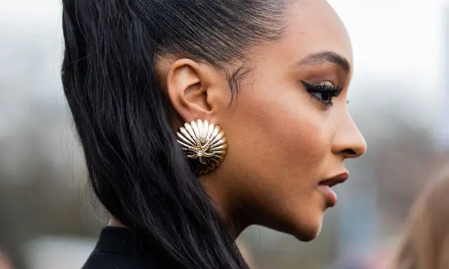 Ein scharfer Cat-Eye-Liner betont die Augen, perfekt aufgetragen mit Kajal. Goldene Muschel-Ohrringe und ein hoher Pferdeschwanz runden den Look ab.