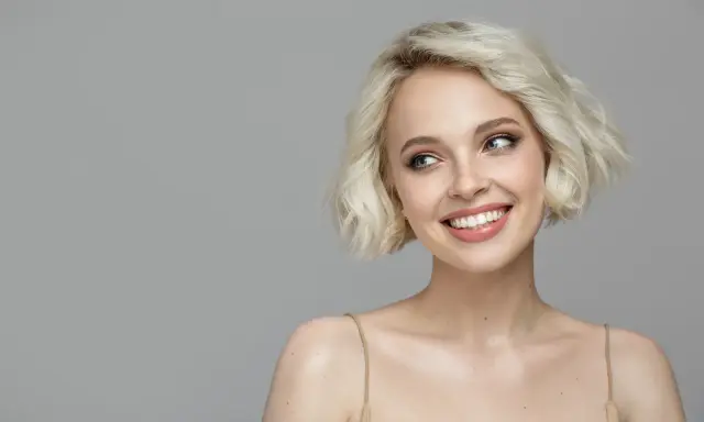 Lächelnde Frau mit sehr feinem Haar, das zu einem kurzen Bob gestylt ist. Ihre blauen Augen blicken nach links.