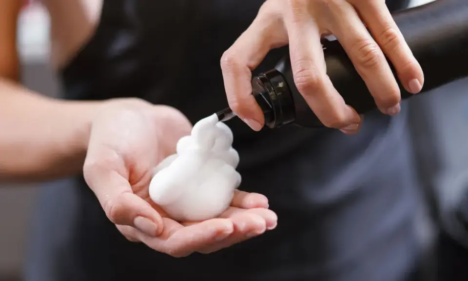 Schaumfestiger Anwendung: Eine Hand hält eine Flasche, aus der weißer Schaum in die andere Hand fließt.