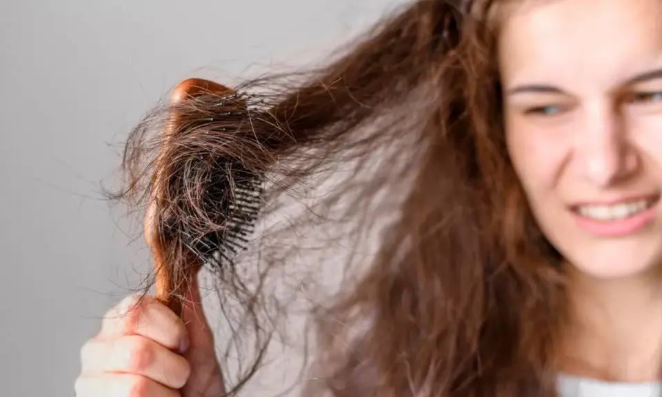 Verzweifelt versucht eine junge Frau, ihre strohigen Haare nach einer Keratinbehandlung zu kämmen. Die Bürste verheddert sich in den widerspenstigen Strähnen.