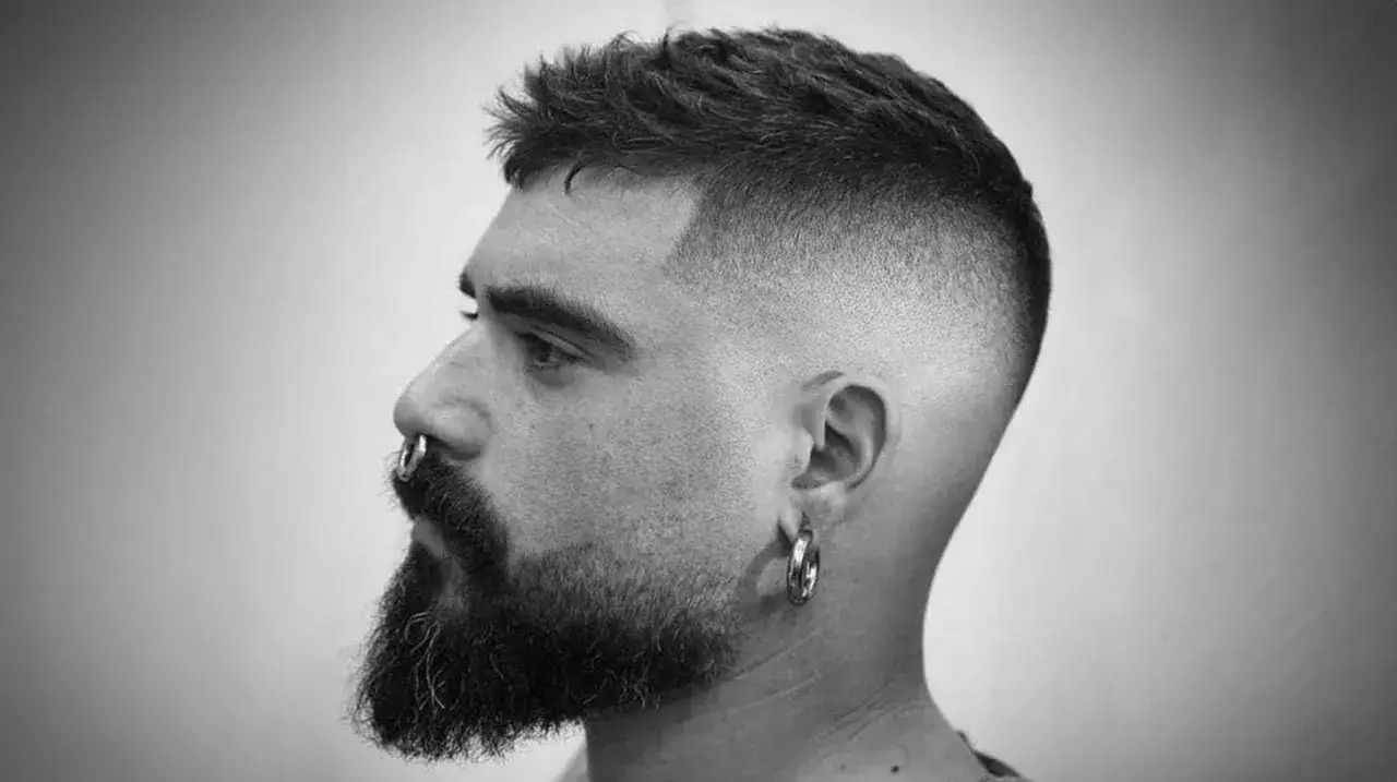 Mann mit Bart und Nasenring, tr&auml;gt einen Buzz Cut Long mit einem sanften Fade.