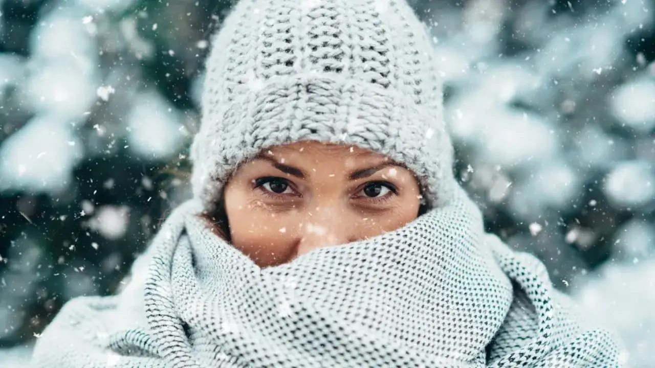 Frau mit M&uuml;tze und Schal, die sich vor der K&auml;lte sch&uuml;tzt. Ihre Augen blicken nachdenklich, w&auml;hrend Schneeflocken fallen und die trockene Haut im Winter betonen.