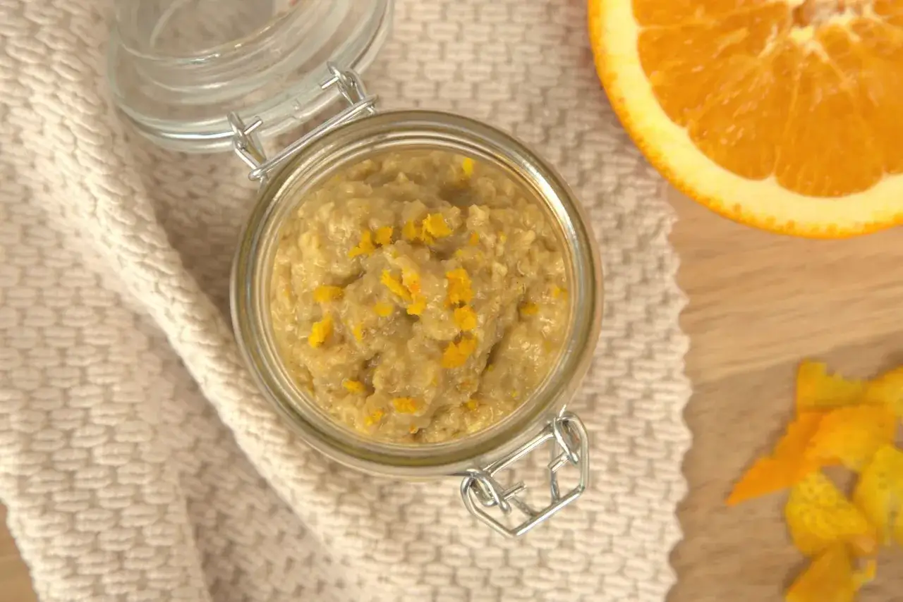 Selbstgemachtes Peeling mit Orangenschale für trockene Haut. Ein Glas mit dem cremigen Peeling steht neben einer Orangenscheibe.