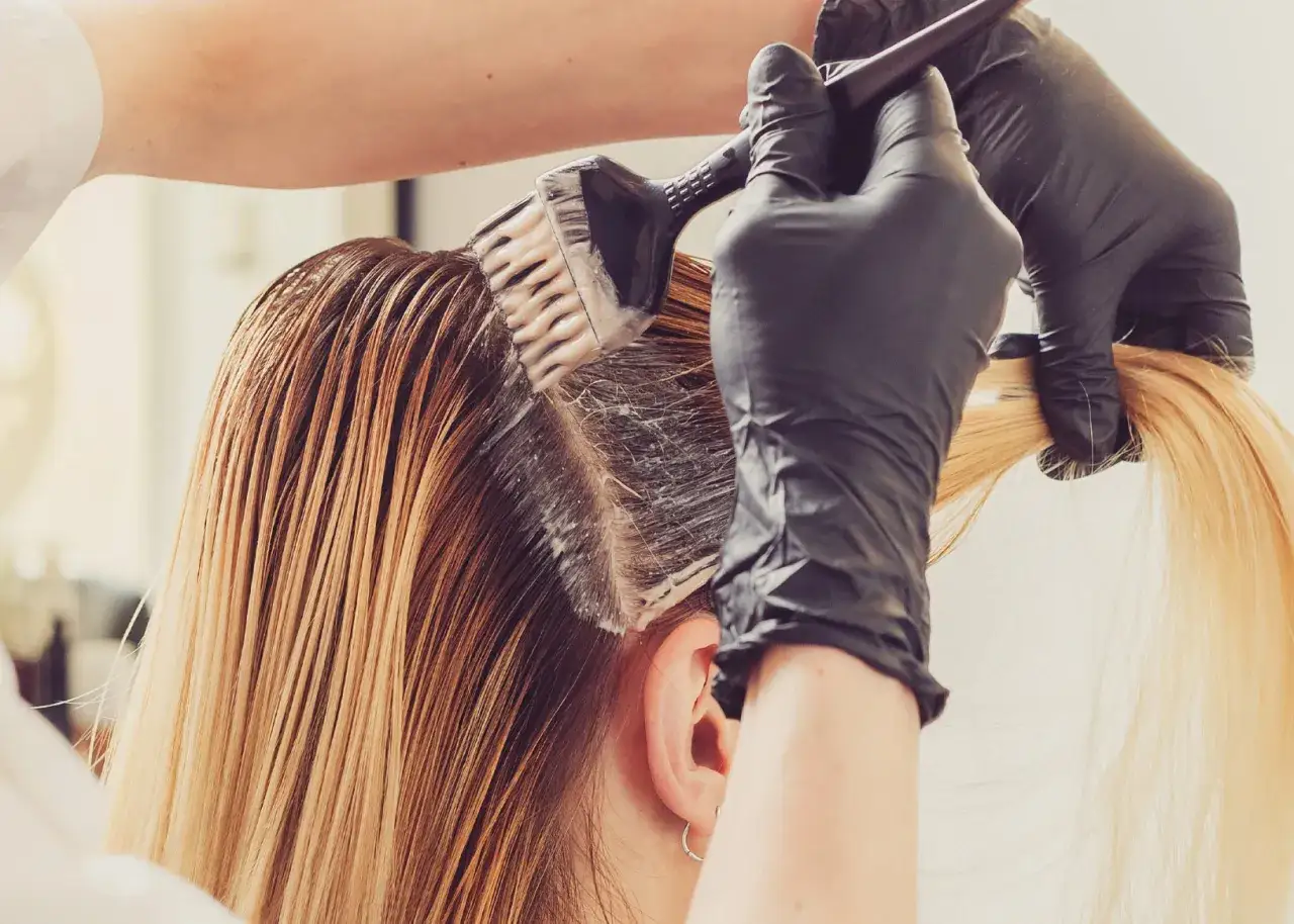 Friseur mit Handschuhen trägt Farbe auf nasses Haar auf, um es zu pflegen und zu verschönern.