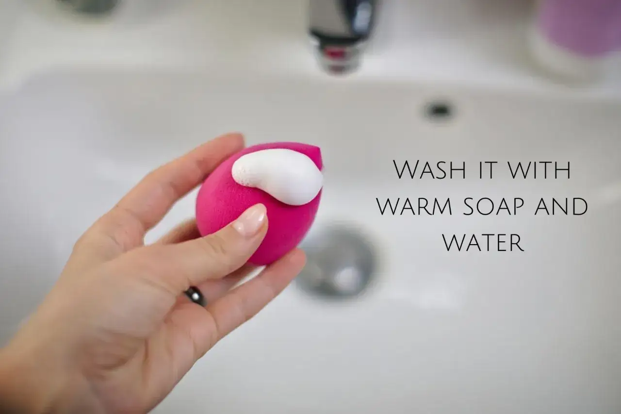 Eine Hand hält einen pinken Make-up-Schwamm mit Schaum. So reinigen Sie ihn mit warmem Seifenwasser.