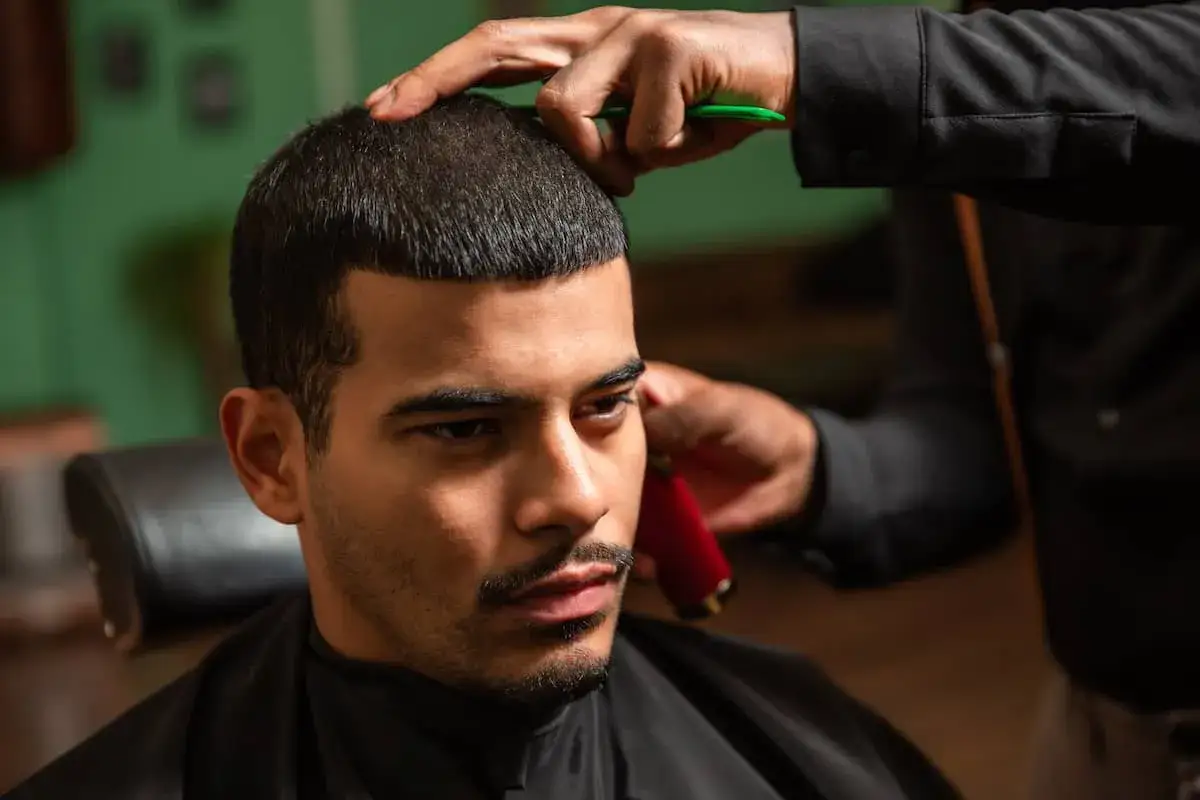 Ein Mann erhält einen präzisen Buzzcut. Der Friseur trimmt das Haar mit einer Schere und einem Trimmer.