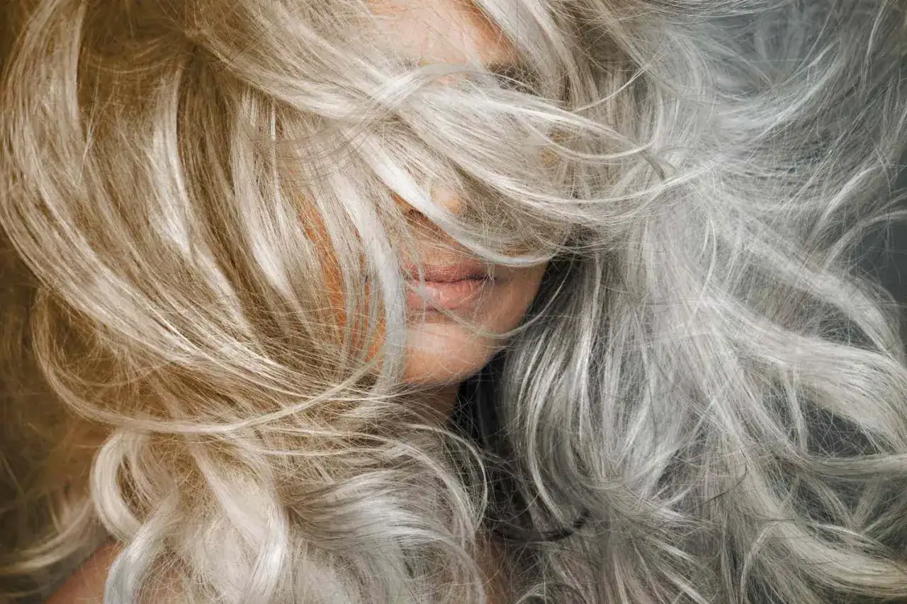Frau mit blonden und grauen Haaren, die ihr Gesicht bedecken. Was tun mit grauen Haaren? Hier sind Ideen für Frisuren.