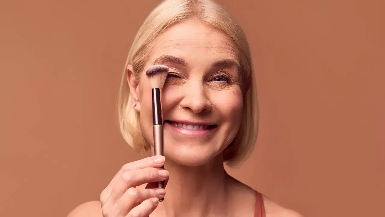 L&auml;chelnde Frau mit Make-up-Pinsel vor dem Auge. Tipps f&uuml;r richtig schminken ab 50.
