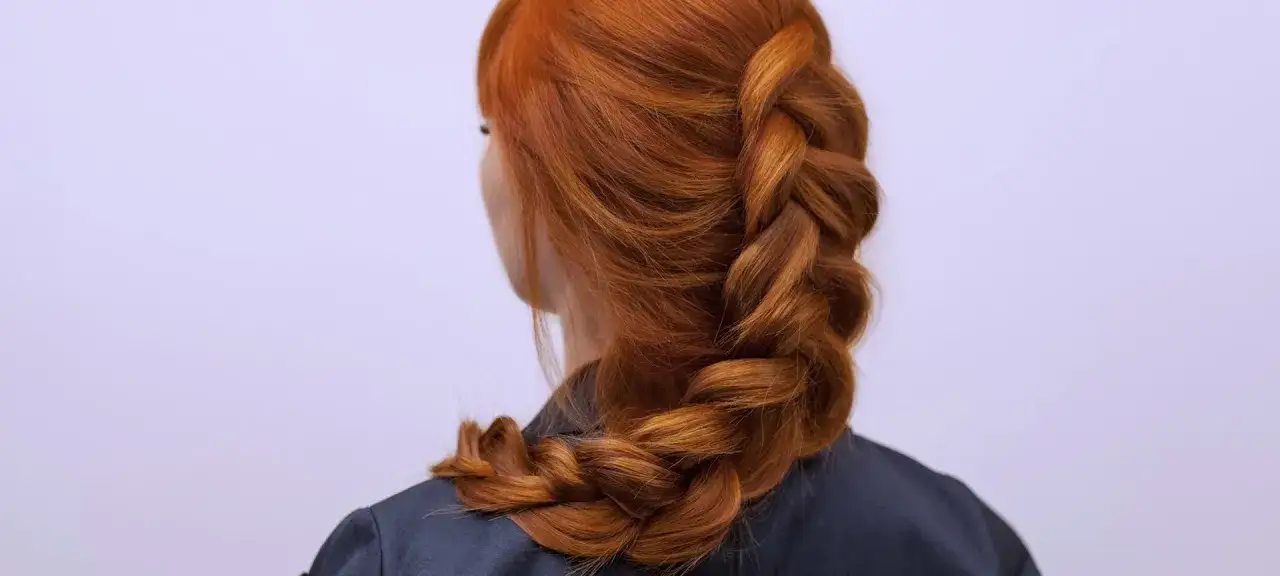 Rotes Haar wird zu einem dicken Bauernzopf geflochten, der elegant über die Schulter fällt.